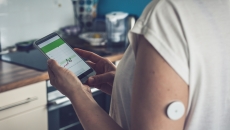 Person wearing a continuous glucose monitor and looking at a phone