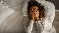 Person lying in bed with their hands over their eyes