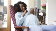 Pregnant person sitting in a chair, looking at a tablet