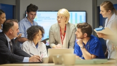 People standing and sitting around a table with a screen showing a graph behind them