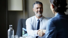 Two people sitting across from each other at a desk shaking hands