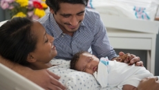 Parents hold infant, one sitting, one laying down