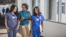 Three healthcare providers walking through a hall while looking at a tablet