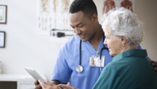 Healthcare provider standing next to a patient and holding a tablet that both individuals are looking at