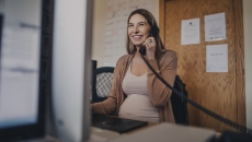 Pregnant person sitting at a desk talking on the phone while looking at a computer