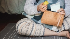 Person pulling period cup and pad out of a brown leather bag