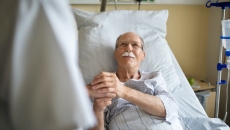 Senior patient holds the hand of a caregiver in hospital bed