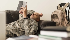 Soldier using digital tablet on sofa near books