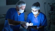 Two people wearing scrubs and masks in a procedure room look at a tablet.