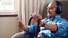 An older man wearing headphones and using a smartphone in his home