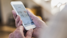 A close-up of a person holding a smartphone displaying heart rate and blood pressure data