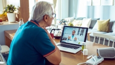 A man talking to a doctor via a laptop with connected devices like a blood pressure cuff and a thermometer