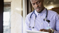 Healthcare provider standing next to a window while looking at a tablet