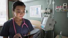 Healthcare provider standing in a hospital room wearing a pink stethoscope while holding a tablet
