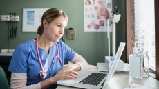 Healthcare provider in scrubs sitting at a desk and looking at a computer