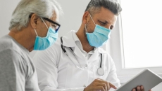 Healthcare provider and patient sitting next to each other wearing masks and looking at a tablet
