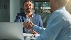 Two people sitting across from each other at a desk and shaking hands