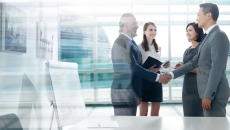 Four people standing in front of a large window with two of them shaking hands and the other two watching