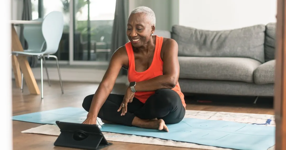 Person sitting on the floor in a room wearing exercise clothes and looking at a tablet