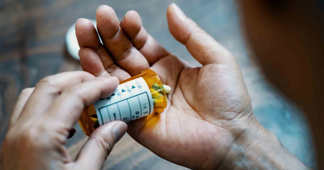 Person holding a pill bottle and pouring medication into their hand