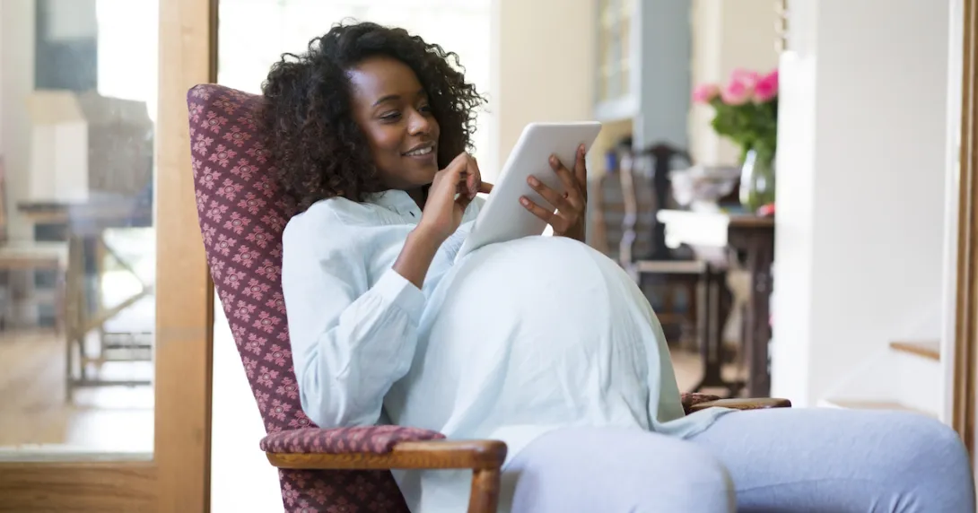 Pregnant person sitting in a chair looking at a tablet