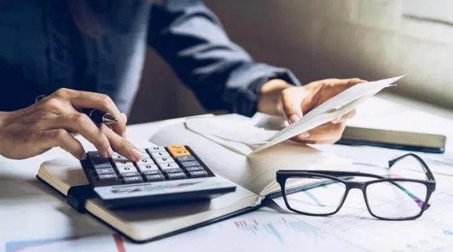Person using calculator with pair of glasses and papers on table