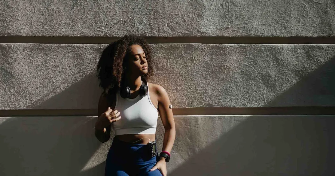 Person wearing a glucose monitor while standing against a wall