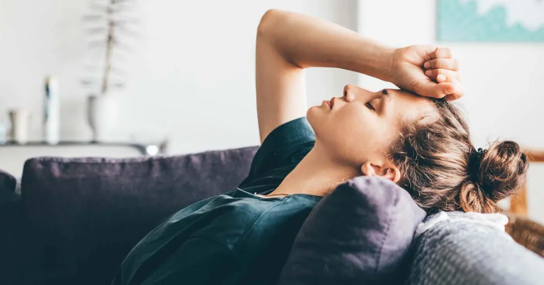 Person lying on a couch with their hand on their forehead with their eyes closed