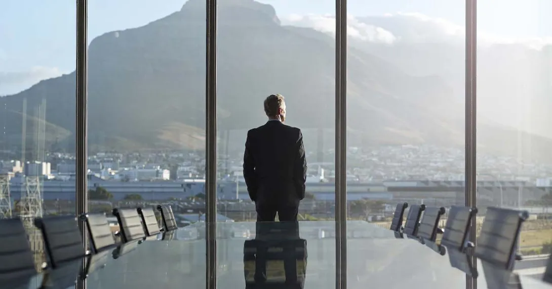 Person standing by a large window with their back turned looking at a large mountain
