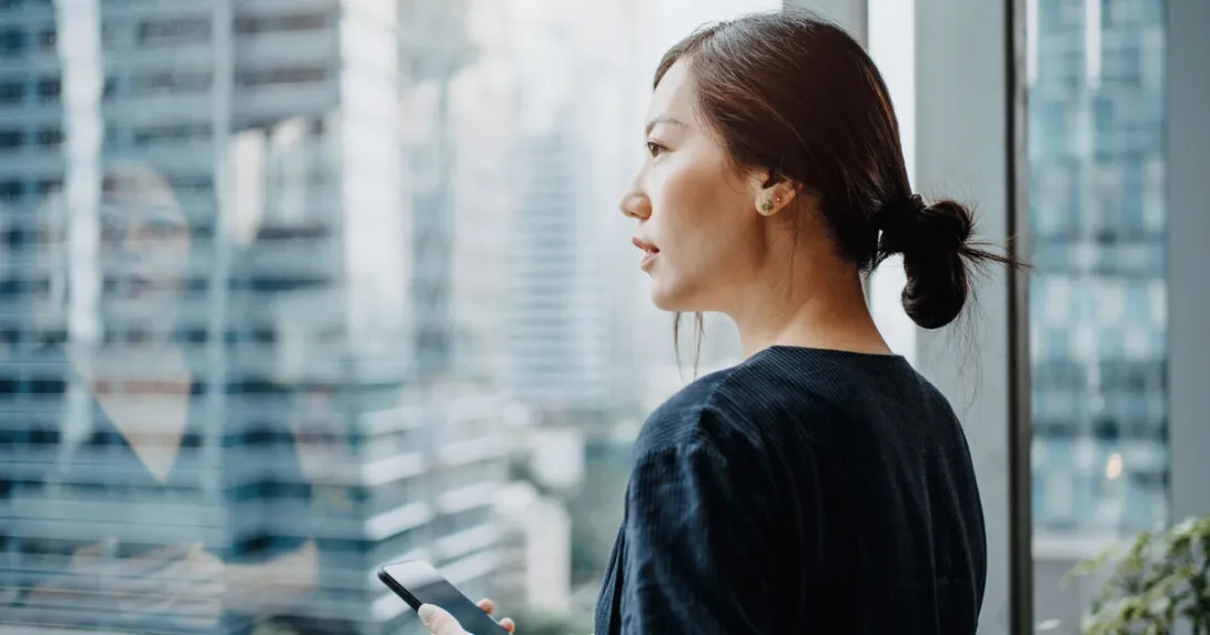 A person holding a smartphone looking out the window