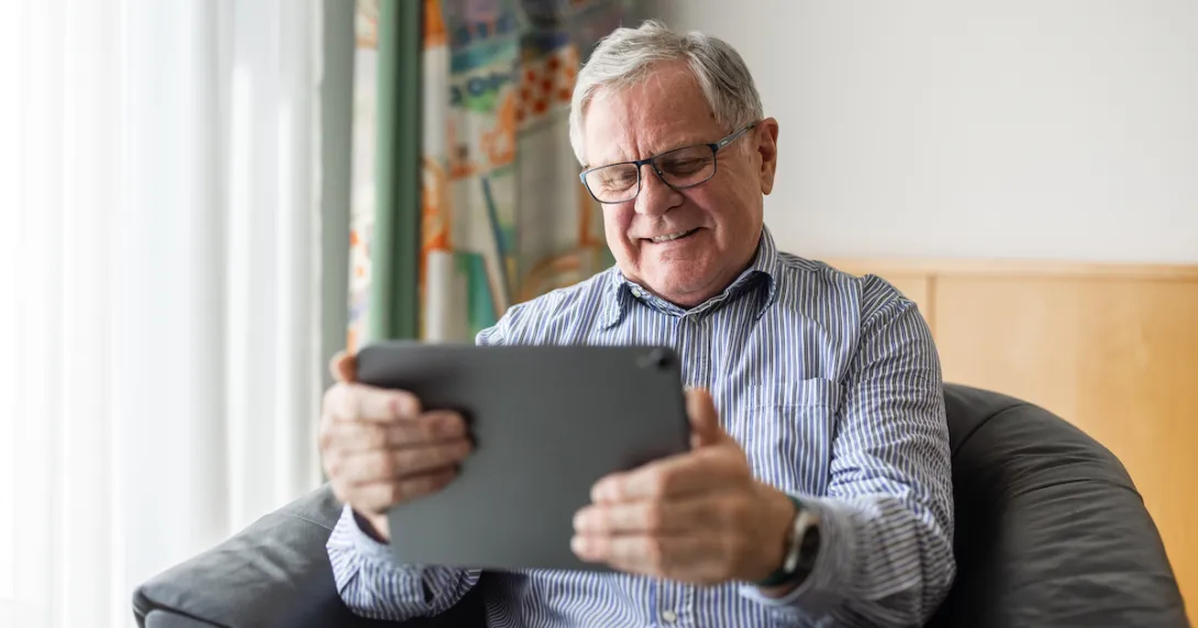 Person sitting in a chair holding a tablet while smiling and wearing glasses