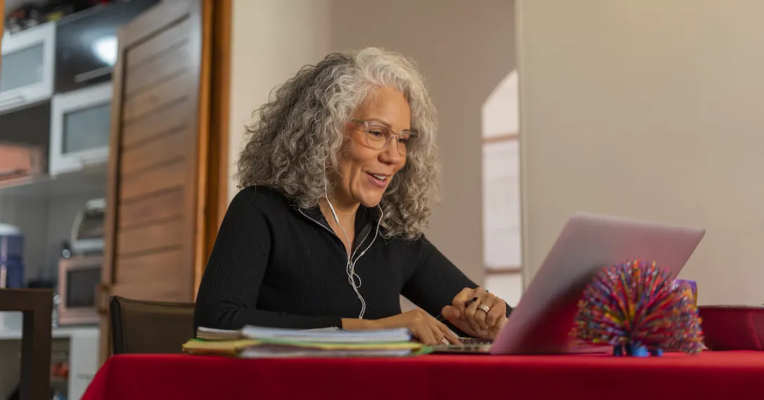 Person sitting at a table with a red table cloth on it while in a home looking at a computer