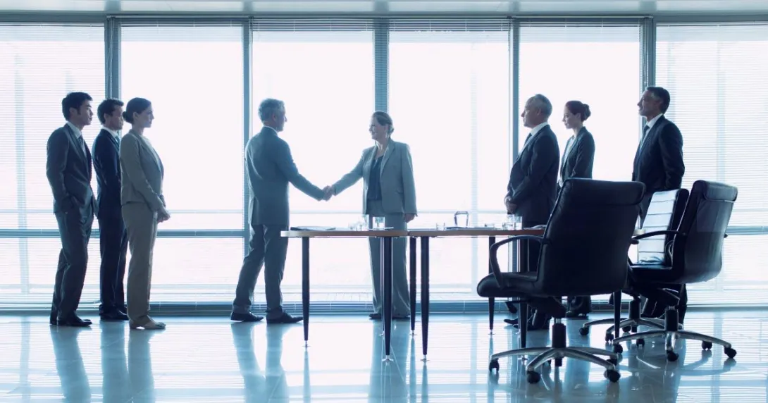 Group of three people on left, two people shaking hands in middle, three people standing behind office chairs on right