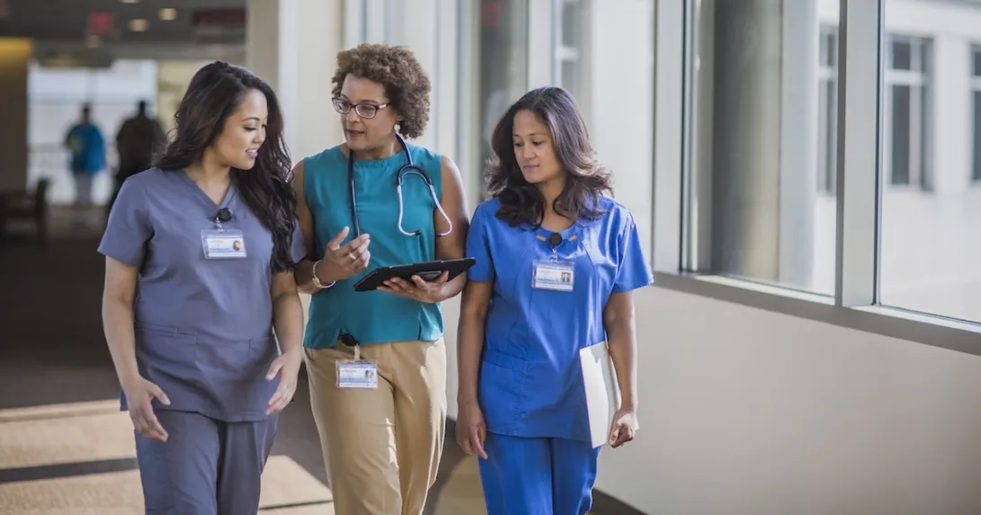 Three people walking down a hall, two healthcare providers in scrubs and one person in civilian clothing