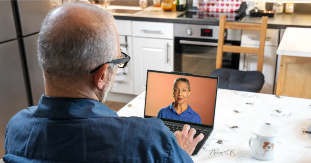 Person sitting at a table while looking at a computer with a person on it