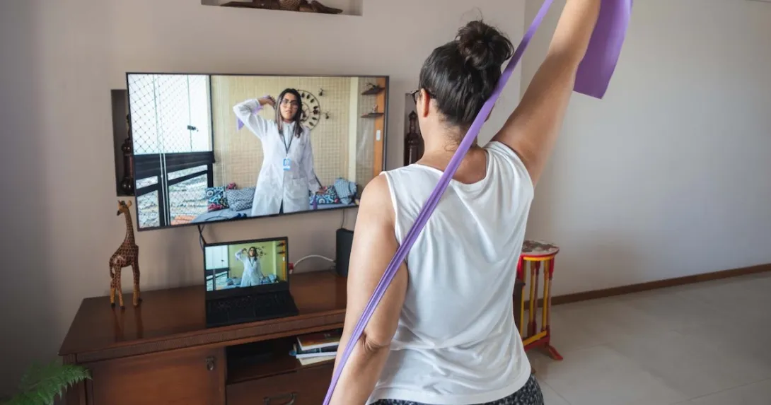 A woman doing exercises guided by a physical therapist on her screen