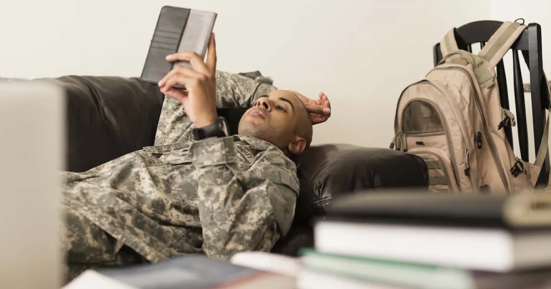 A soldier using a tablet while lying on a sofa.