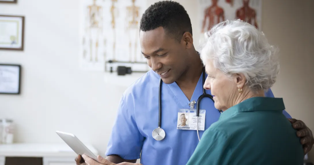 A doctor and a patient look at a tablet in his office.