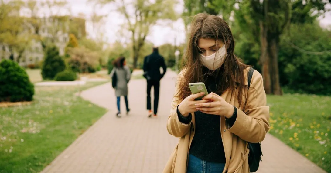 A person wearing mask is typing on their phone