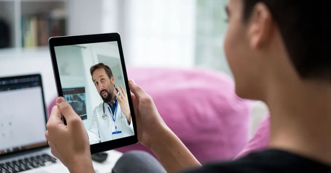 Person sitting in a room while holding a tablet that has a healthcare provider on the screen