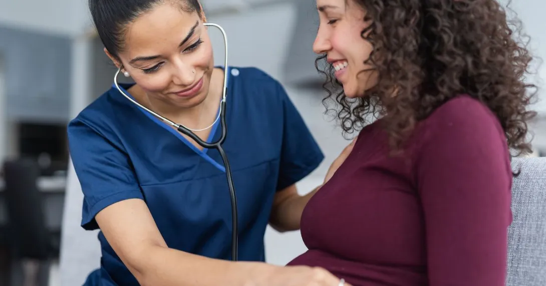 Healthcare professional listening to a pregnant person's stomach with a stethoscope
