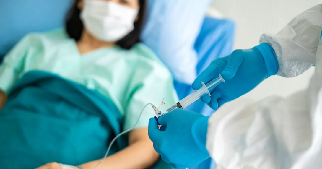 Healthcare provider putting medication into an infusion line with a patient lying in a bed