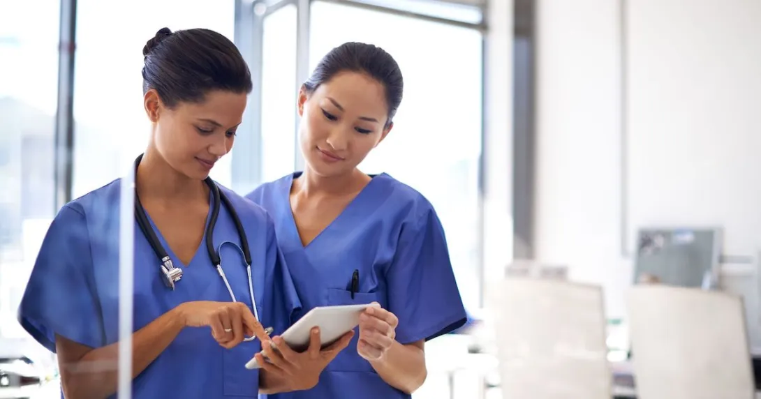 Two healthcare professionals standing next to each other while looking at a tablet