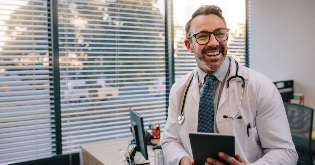 Healthcare provider sitting on a desk holding a tablet while smiling