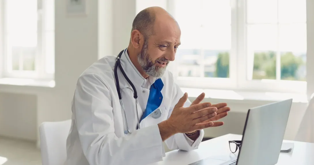 Healthcare provider sitting at a desk and talking to someone on a computer