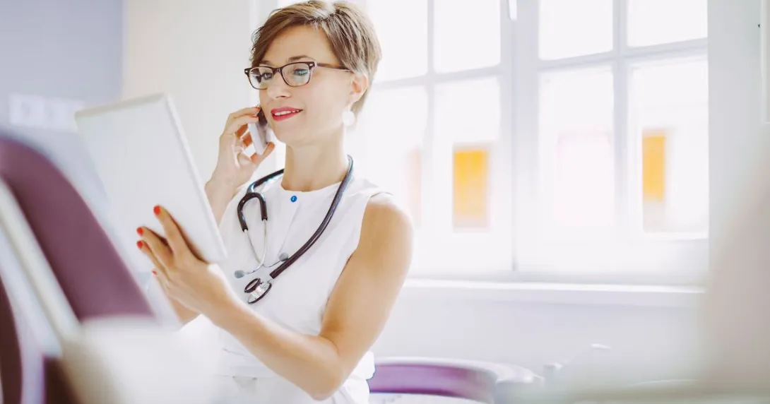 Healthcare provider looking at a tablet while wearing a white shirt and a stethoscope around their neck