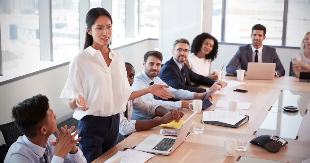 Several people sitting in a board room looking at one person standing up