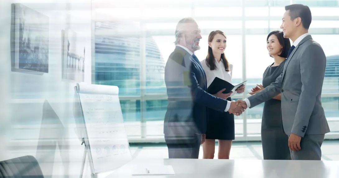 Two people shaking hands with two more people watching