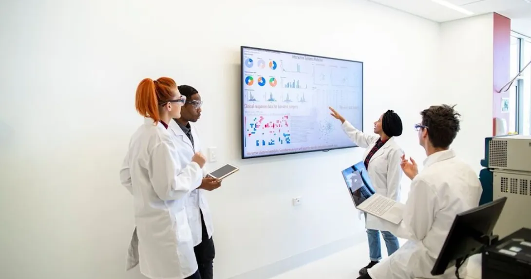 Four healthcare providers in a room looking at a screen with data on it