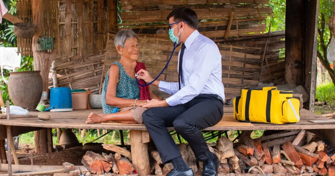 A rural doctor checking an elderly person's breathing with a stethoscope in a hut